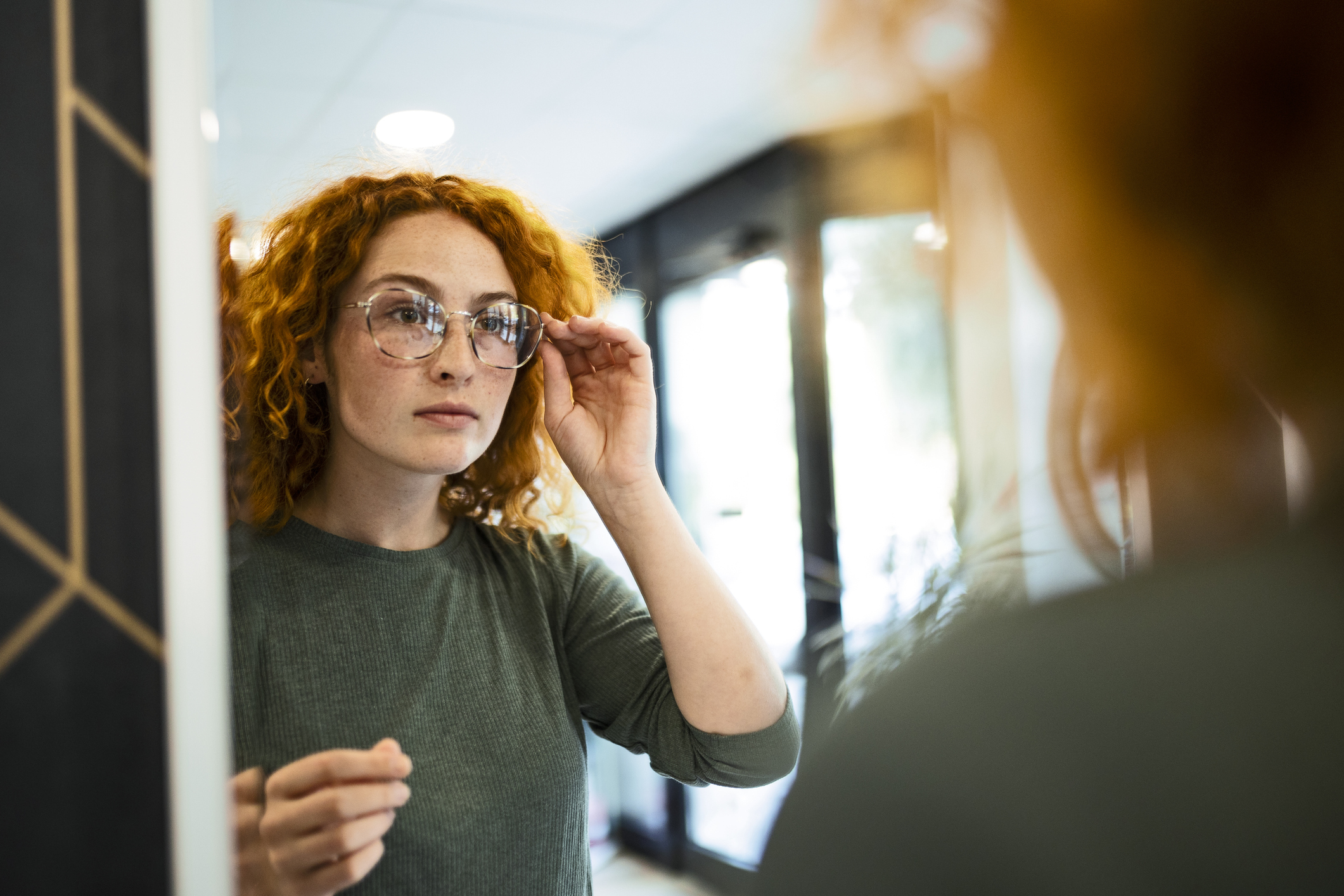 Young woman trying on glasses in optical store looking at mirror Young woman trying on glasses in optical store looking at mirror